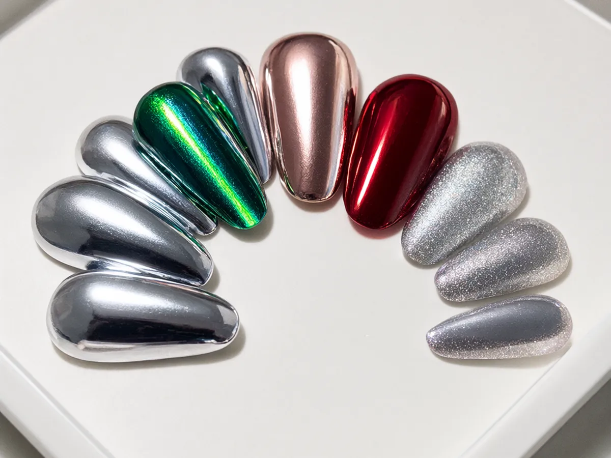 Almond nail tips in silver chrome, emerald cat-eye, rose-gold chrome, cherry red and silver glitter on a white tray